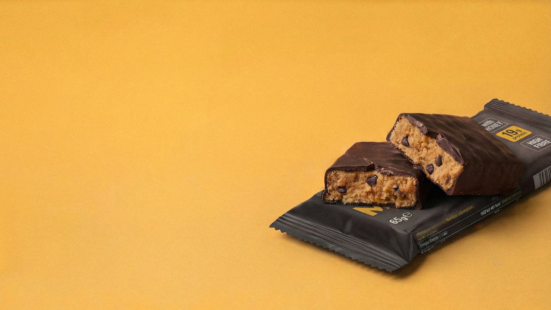 Mighty Bar peanut butter protein bar, opened to show the chocolate and peanut interior, on a warm orange background
