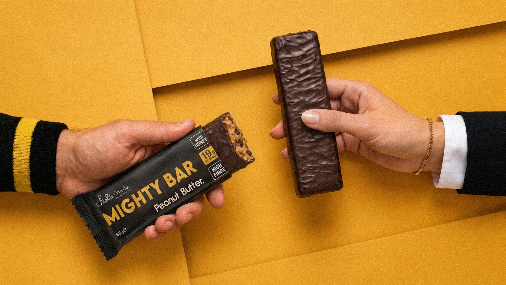 Two hands holding Mighty Bar — one still wrapped, one unwrapped — on an orange background