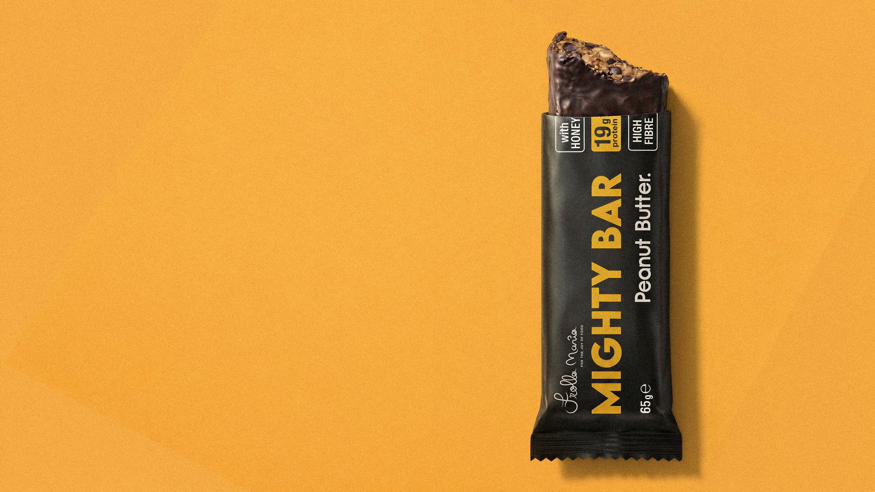 Mighty Bar peanut butter protein bar, partially unwrapped showing the chocolate and peanut interior, on a warm orange background