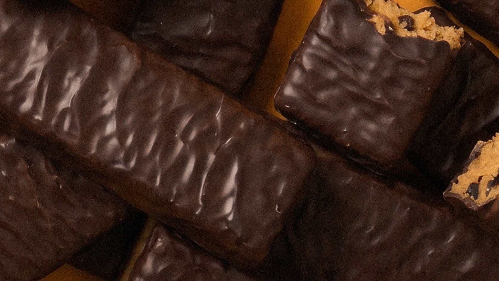 A pile of Mighty Bar protein bars coated in dark chocolate, some broken open to show the peanut butter centre